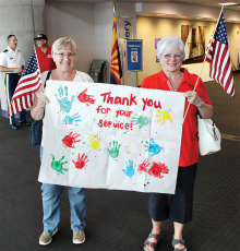 Shelia Parks (left) and Karen Woodrow hold up a banner thanking World War II veterans for their service. The banner was made by Sheila and Drew Parks’ four year old granddaughter’s Montessori preschool class in Lake Forest, California; photo by John McGee.