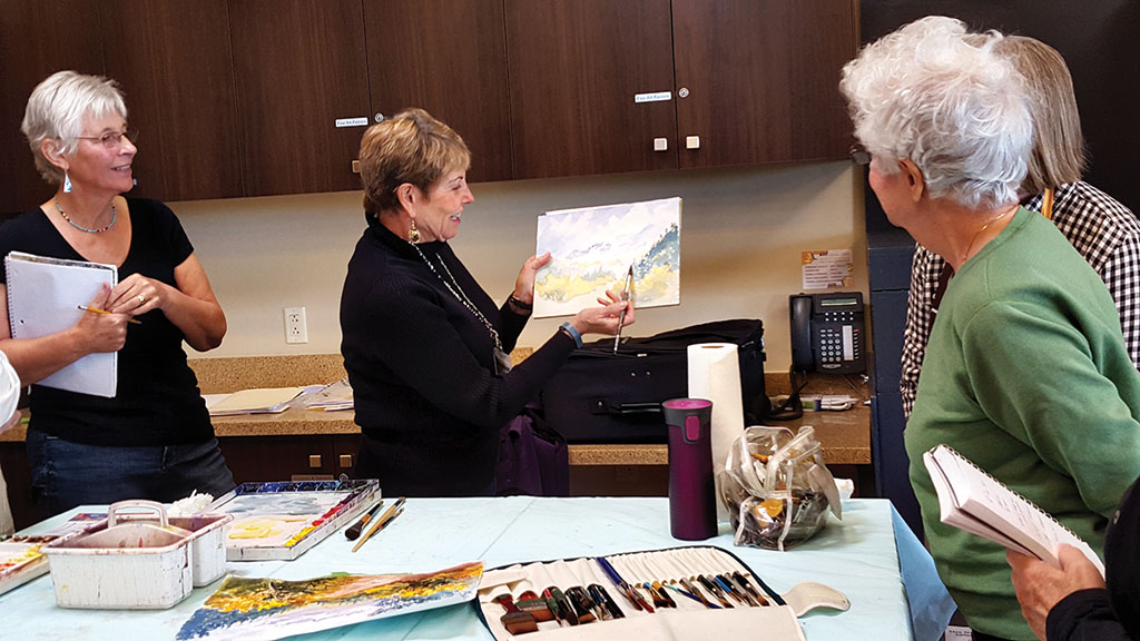 Resident Jean Pastore demonstrates watercolor painting with students attending her recent class. Jean will teach basic watercolor technique again in a Come and Try It workshop on January 14.