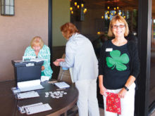 With a big green shamrock on her shirt, Ginny McGinnis gives out the hole assignment numbers to the Lady Putters; photo by Sylvia Butler.