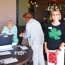 With a big green shamrock on her shirt, Ginny McGinnis gives out the hole assignment numbers to the Lady Putters; photo by Sylvia Butler.