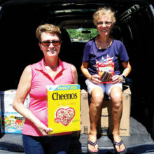 Left to right: Barbara Gavre and Peggy McGee show off just some of the grocery items that were donated during the Food for the Troops drive; photo by John McGee