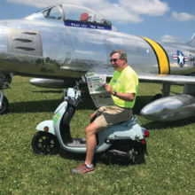 Bill Foraker relaxes in front of an F86 Sabre fighter jet while working the Warbirds area of EAA Oshkosh Airventure 2019.